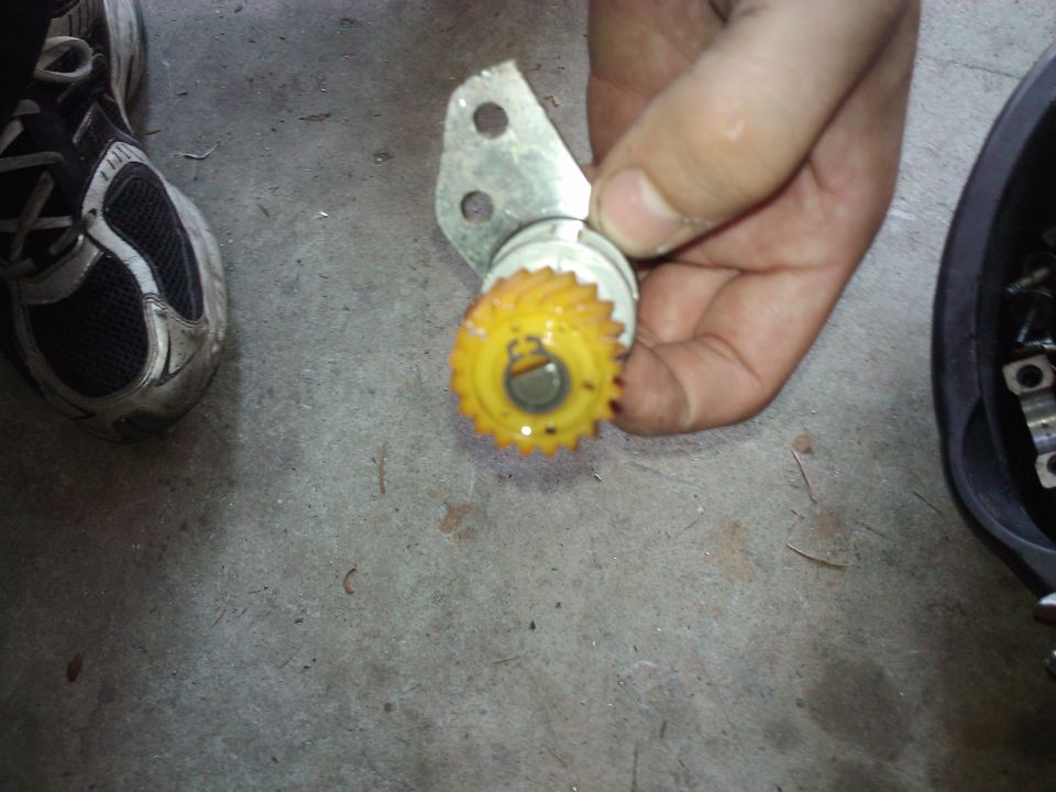 Hand holding a yellow plastic speedometer gear with a metal bracket