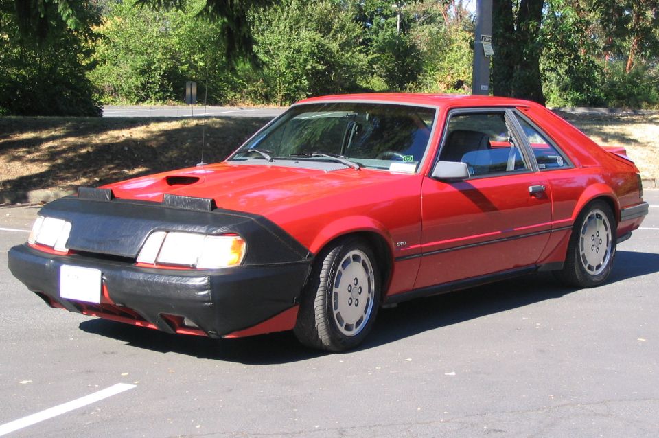 Red Fox-body Mustang hatchback with black front bra and hood scoop, front three-quarter