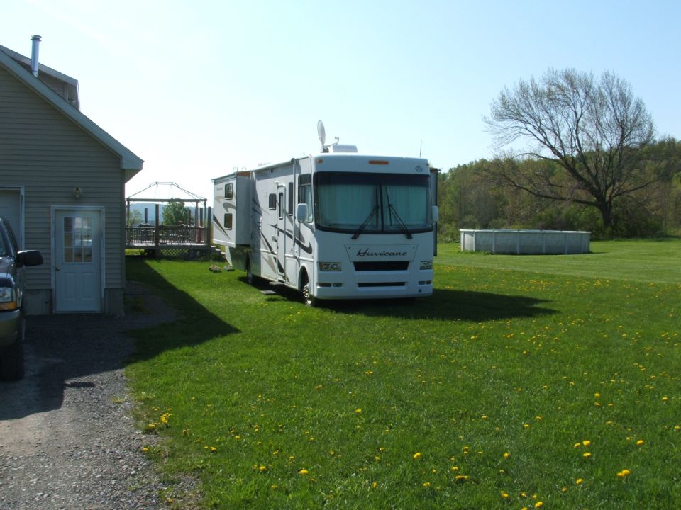 White RV with slide-out parked on a grassy lawn next to a house