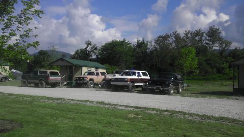 1989 Ford Bronco - A group of SUVs are parked outside a small building on a sunny day with clouds in the sky.