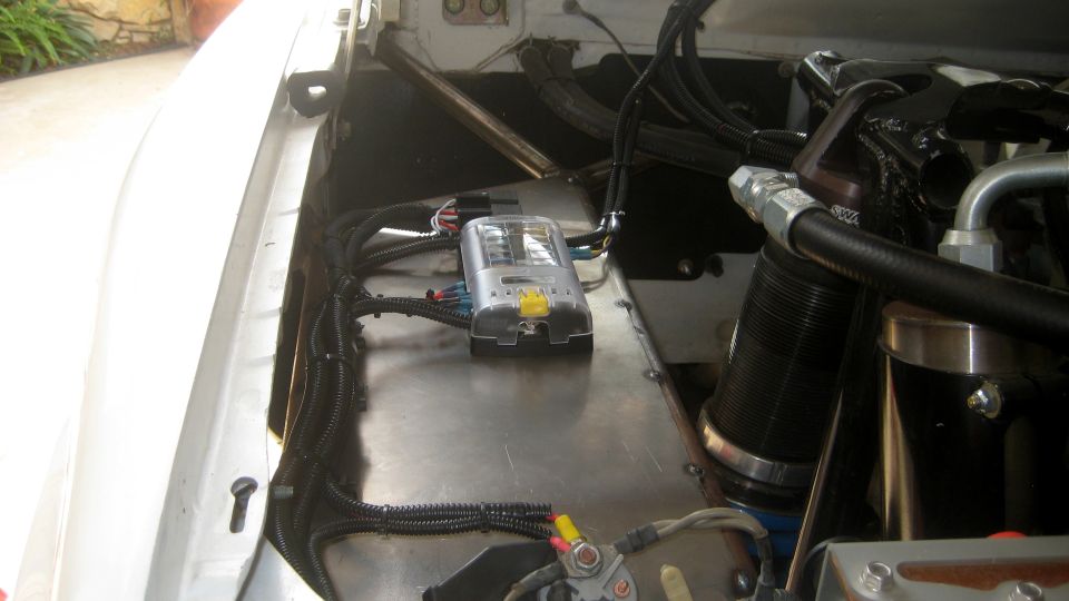 Engine bay with a silver fuse box and black wiring harnesses. Some metal sheeting is visible