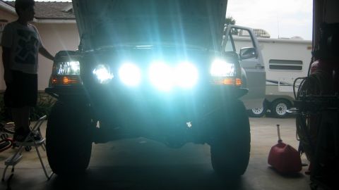1996 Ford Bronco - The front of a 1996 Ford Bronco is illuminated by its bright headlights, with a person standing nearby.