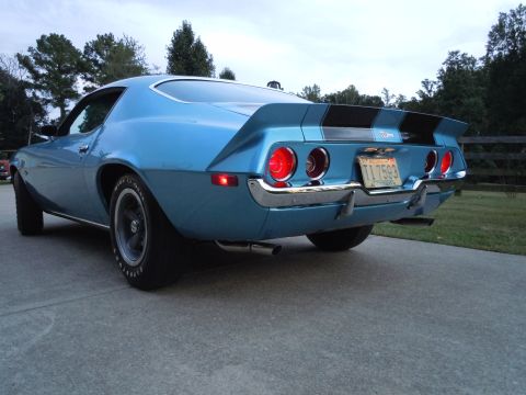 1972 Chevrolet Camaro - The rear of a blue Chevrolet Camaro is shown with dual taillights and a spoiler. A license plate is visible on the rear bumper.