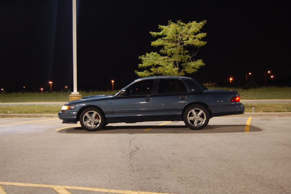 Blue sedan parked in a lot at night, tree in background