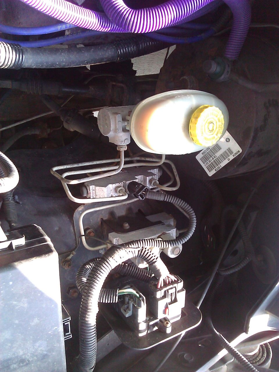 Brake fluid reservoir and master cylinder assembly with hoses and wiring. Label visible on reservoir