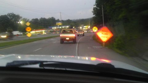 1989 Ford Bronco - A tan pickup truck with a white stripe is seen from behind on a highway as traffic passes by during dusk.