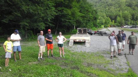 1989 Ford Bronco - A group of people gather near a flatbed trailer in a scenic, wooded location.