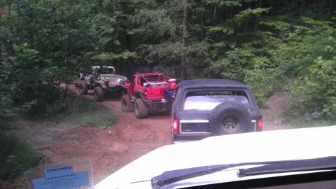 1989 Ford Bronco - Multiple off-road vehicles, including a 1989 Ford Bronco, travel on a wooded dirt path.