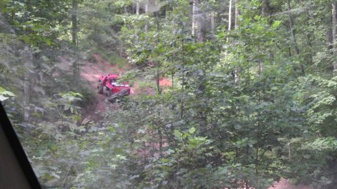 1989 Ford Bronco - A red off-road vehicle navigates a wooded trail.