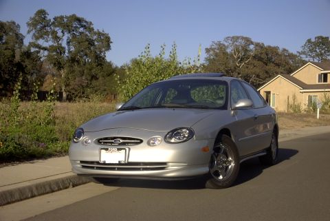 1998 Ford Taurus - Silver 1998 Ford Taurus sedan parked on a residential street with a house in the background.