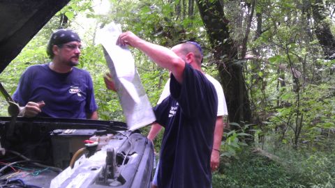 1989 Ford Bronco - Two men consult a map with the hood of a vehicle open in a wooded area.