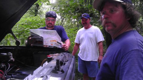 1989 Ford Bronco - Three men consult a map near an open truck engine in a wooded area.