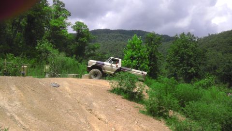 1989 Ford Bronco - Pickup truck navigates an off-road trail with wooded hills in the background.