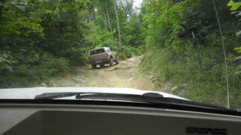 1989 Ford Bronco - A 1989 Ford Bronco navigates a challenging, rocky path through a wooded area.
