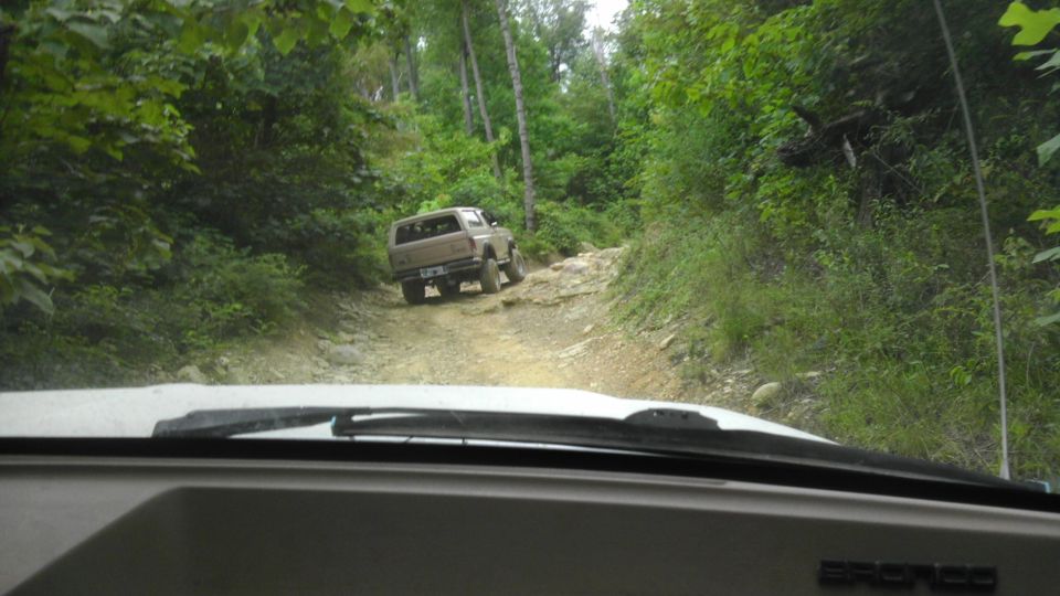 Brown 1989 Ford Bronco driving on a rocky dirt road, seen from another vehicle's interior