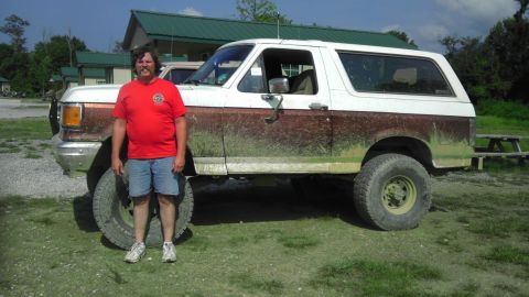 1989 Ford Bronco - A man poses with his lifted Ford Bronco, which appears to be covered in mud from off-roading.