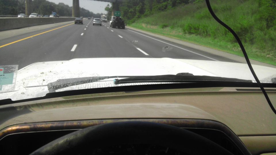 View from inside a vehicle looking out at a highway with other cars. Dashboard and windshield wipers visible