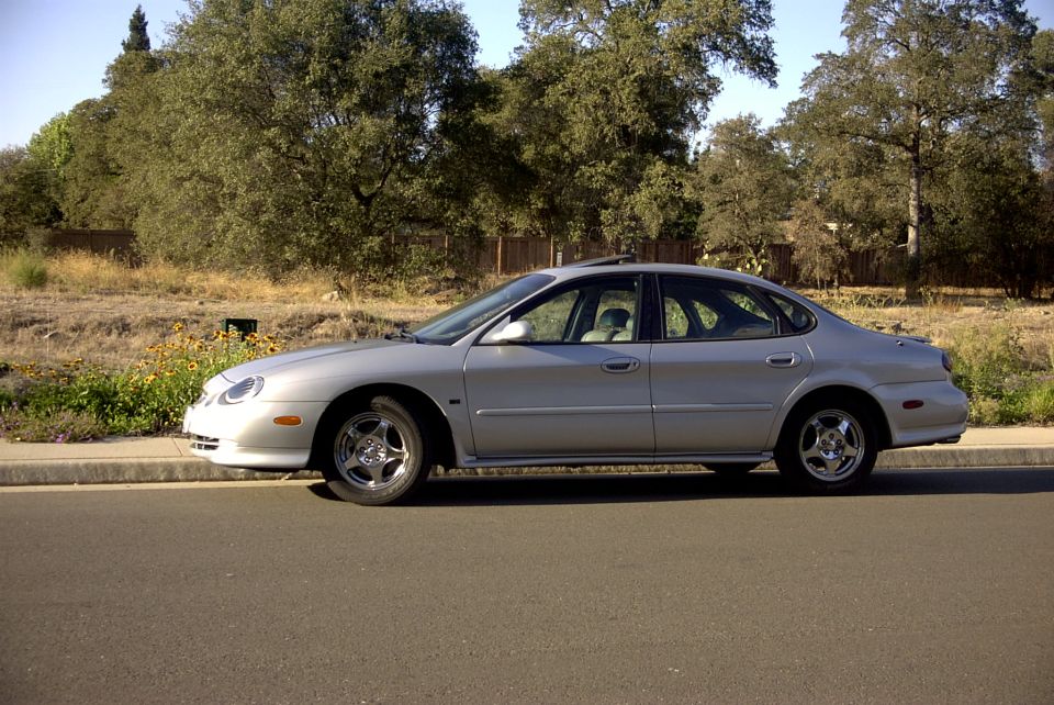 silver sedan parked on street, trees and dry grass in background