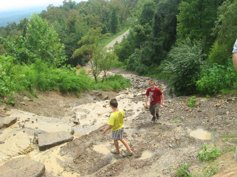 1990 Ford Bronco - Two boys navigate a challenging muddy and rocky trail in a wooded area.