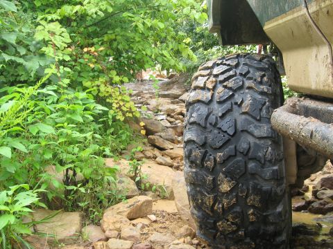 1990 Ford Bronco - Off-road tire navigating a challenging rocky path. The vehicle's body is partially visible.