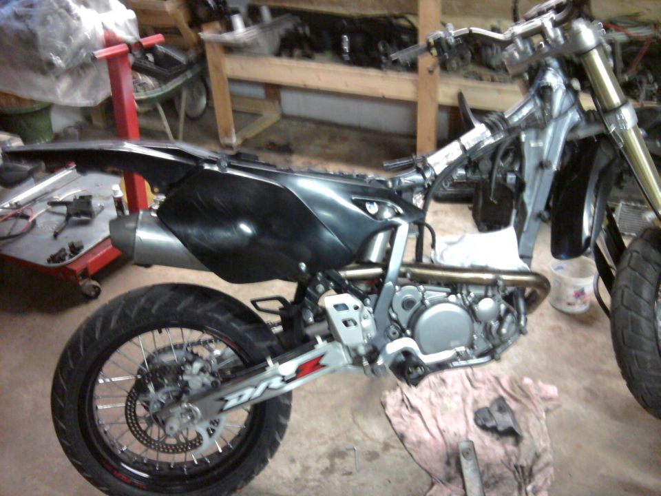 2007 Suzuki DR-Z400S motorcycle side view, black body panels, silver frame, in a workshop