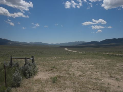 1989 Ford Bronco - Expansive rural landscape with a dirt road leading into the distance, framed by a fence and mountains.