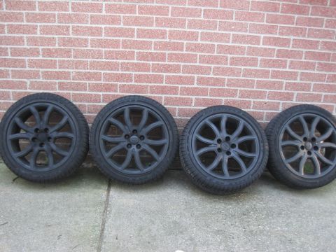 2010 Ford Fusion - A set of four black alloy wheels and tires are displayed in front of a brick wall.