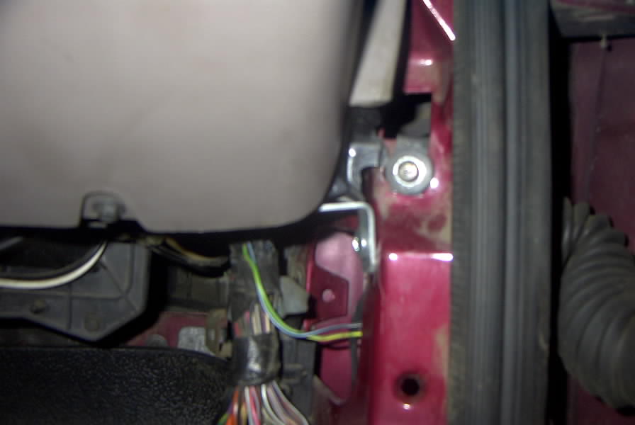 Close-up of maroon body pillar, bolt, and exposed wiring inside a vehicle under repair