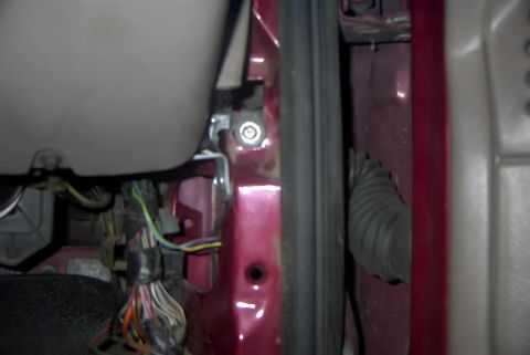 1994 Ford Bronco - Close-up of an open door jamb and A-pillar on a maroon vehicle, showing a multicolored wiring harness, the door striker bolt, weatherstripp…