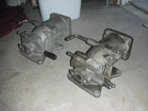 1998 Ford Crown Victoria - pair of matching cast-aluminum mechanical housings with mounting flanges and protruding ports sit on a gray concrete floor.
