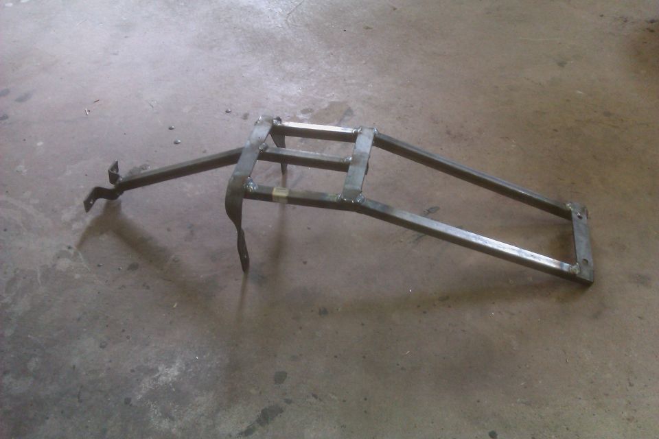 Metal luggage rack with welded joints and mounting brackets, resting on a concrete floor