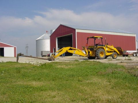 1992 Ford Bronco - A yellow backhoe loader is parked on a farm in front of a large red barn.