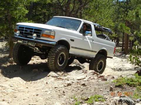 1996 Ford Bronco - A white 1996 Ford Bronco navigates a challenging rocky terrain on an off-road trail.