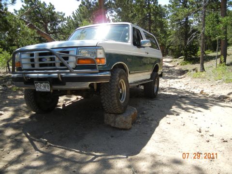 1996 Ford Bronco - 1996 Ford Bronco navigates a rough, rocky trail in a wooded area.