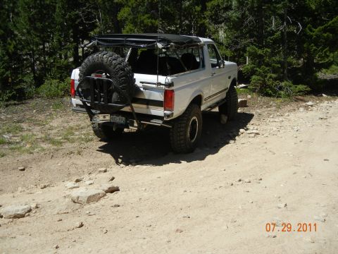 1996 Ford Bronco - A white Ford Bronco is parked on a dirt road with trees in the background.