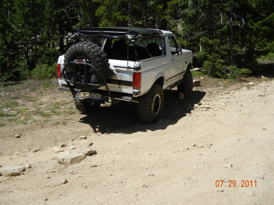 White Ford Bronco with a roof rack and rear-mounted spare tire on a dirt road