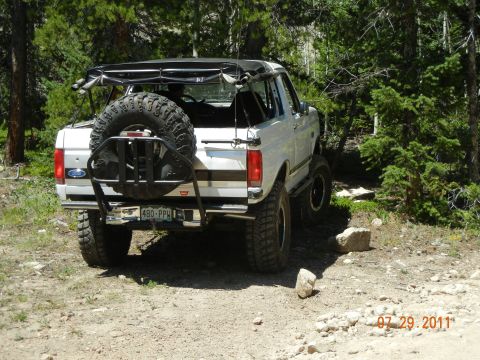 1996 Ford Bronco - 1996 Ford Bronco seen off-roading on a dirt trail with trees in the background.