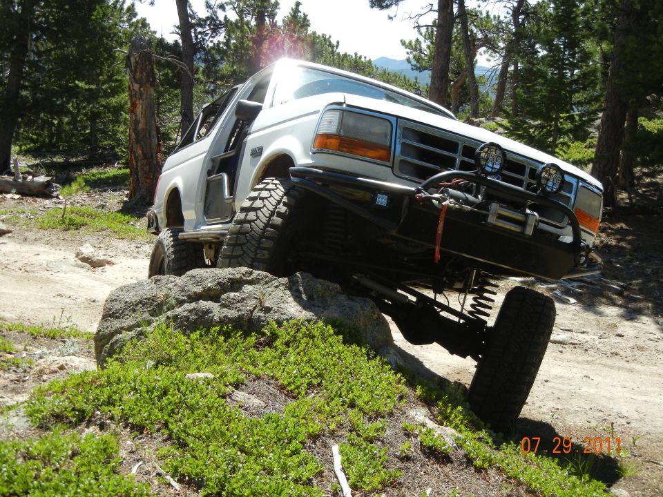 White SUV with lifted suspension and large tires climbing over a rock on a dirt trail