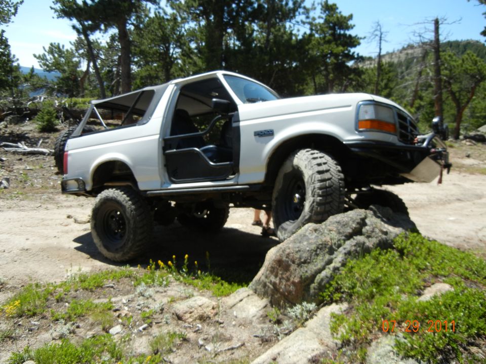 White Ford Bronco with doors removed, climbing over rocks on a dirt trail