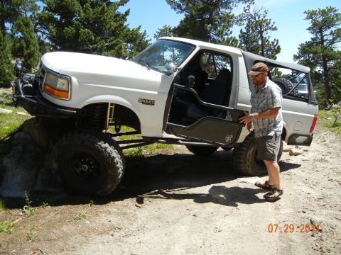 1996 Ford Bronco - A white 1996 Ford Bronco is shown with its door open, modified for off-road use on a dirt path.