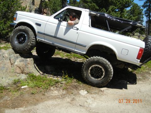 1996 Ford Bronco - A white 1996 Ford Bronco navigates a rocky trail, its off-road capabilities.