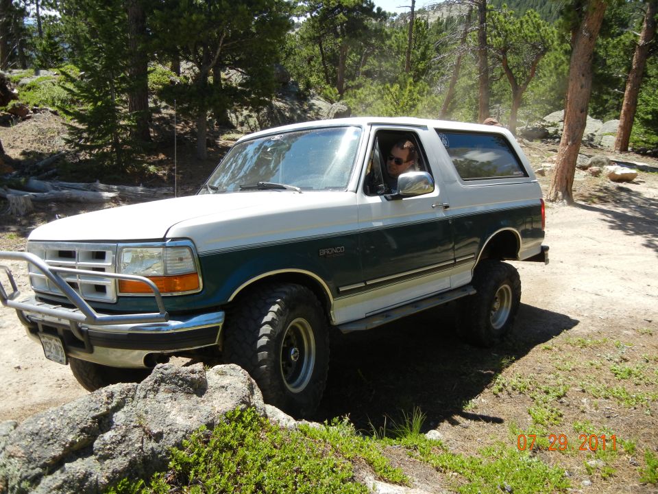 1996 Ford Bronco on a dirt trail with trees and rocks