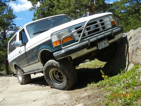 1996 Ford Bronco - A white and green 1996 Ford Bronco navigates a rocky trail, demonstrating its off-road capabilities.