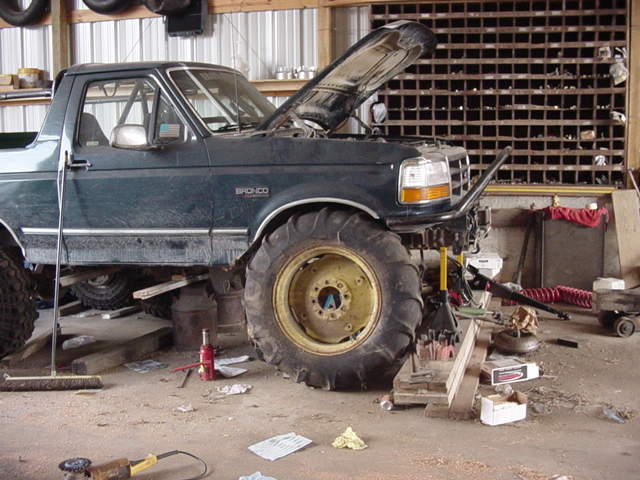 1992 Ford Bronco with large tires, hood up, in a workshop. It is on jack stands