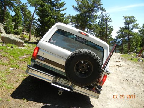 1996 Ford Bronco - A 1996 Ford Bronco is seen from the rear, parked on a dirt road with trees and rocks in the background.
