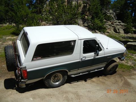 1996 Ford Bronco - Two-tone 1996 Ford Bronco parked outdoors on a dirt path with trees and rocks in the background.