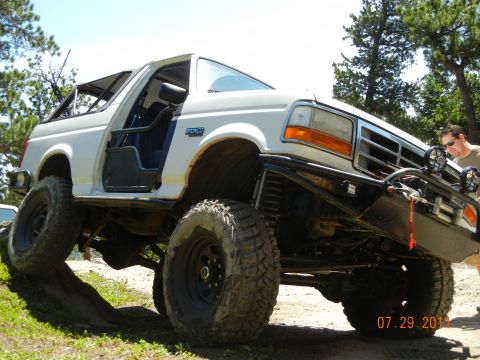 1996 Ford Bronco - A white 1996 Ford Bronco is shown off-roading on a sunny day with a man standing nearby.