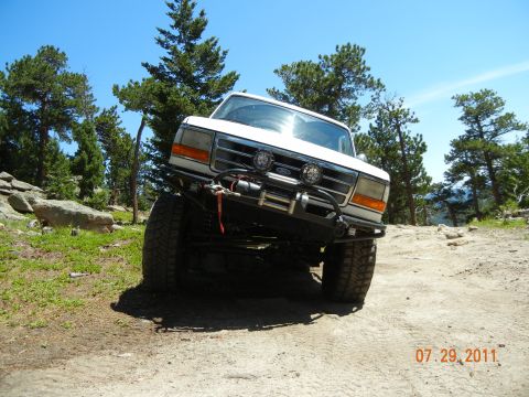 1996 Ford Bronco - A white Ford truck navigates a rocky, off-road trail under a clear blue sky.