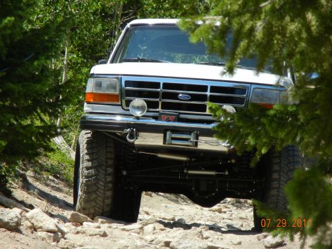 1996 Ford Bronco - A white 1996 Ford Bronco navigates a rocky trail, seen from the front with a winch mounted on the bumper.