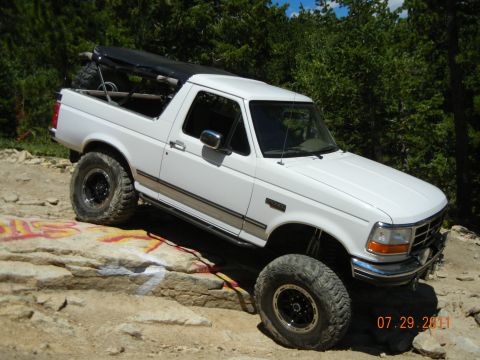 1996 Ford Bronco - This white 1996 Ford Bronco is shown off-roading on a rocky terrain with a clear blue sky above.